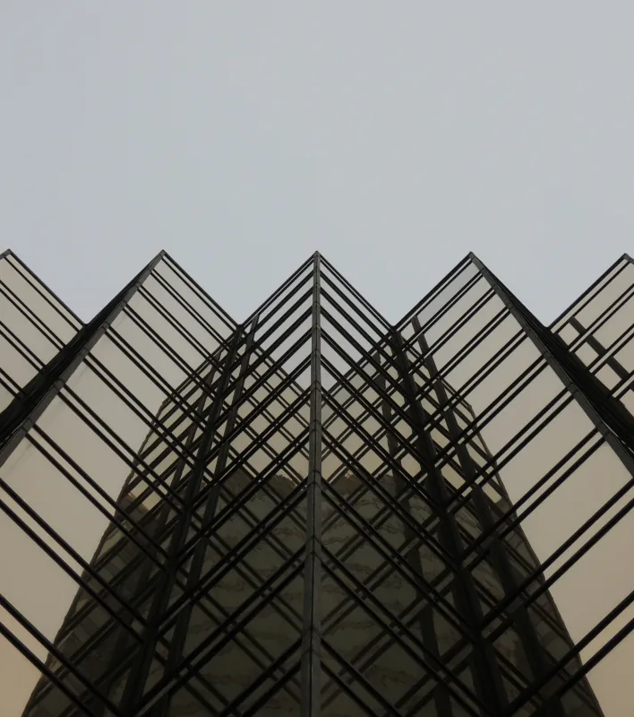 Black steel-and-glass building with repeating triangular frames seen from below