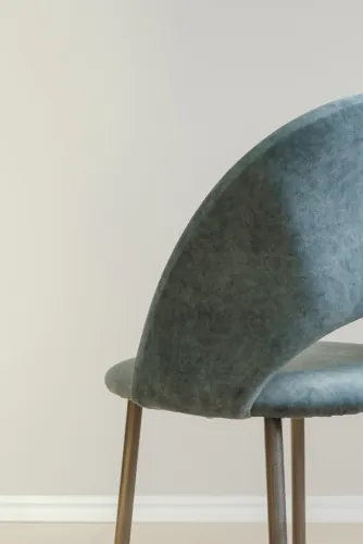 Blue-green velvet chair with wooden legs against a cream wall