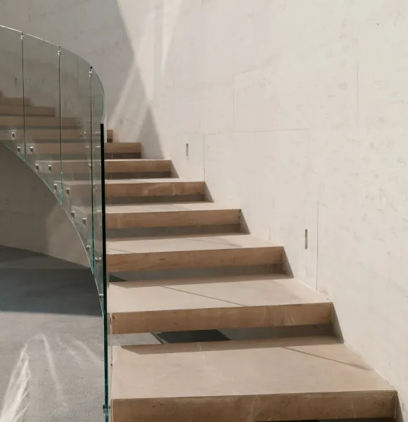 Floating stone staircase with a glass balustrade against a pale wall
