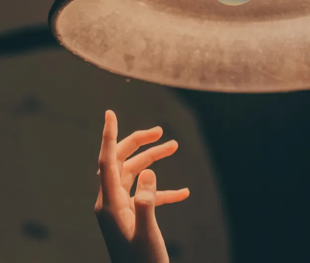 Hand reaching up beneath a warm-lit lampshade