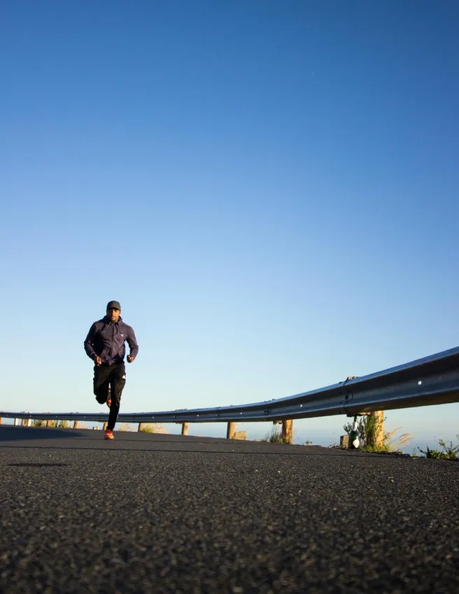 Man running along a coastal road under a clear blue sky