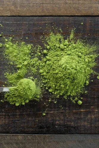 Bright green matcha powder scattered on a dark wooden table