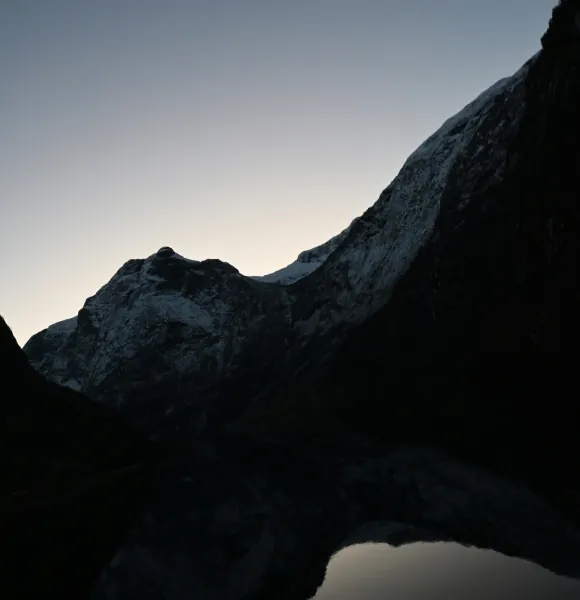 Dark mountain ridge silhouetted at dusk above still water