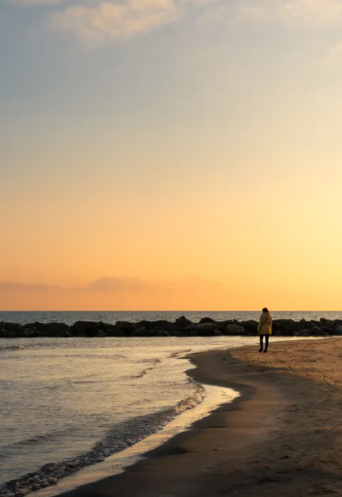 Lone person walking along a curving beach at sunset