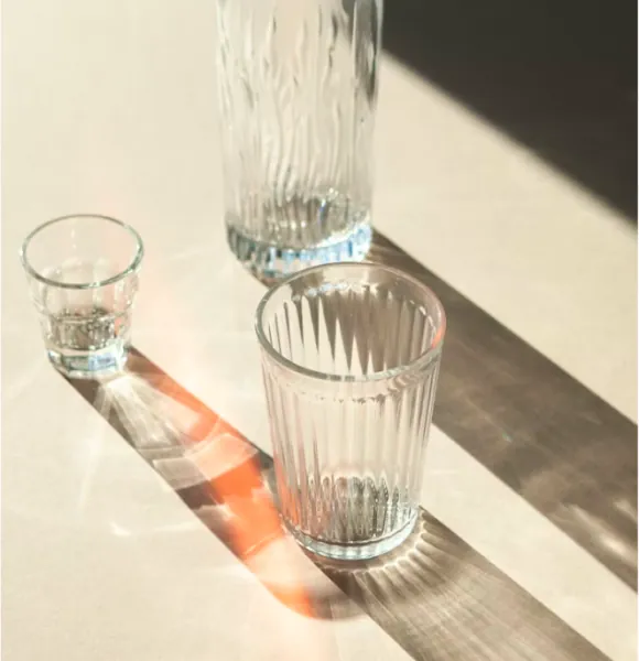 Ribbed drinking glasses and a carafe casting long shadows in sunlight