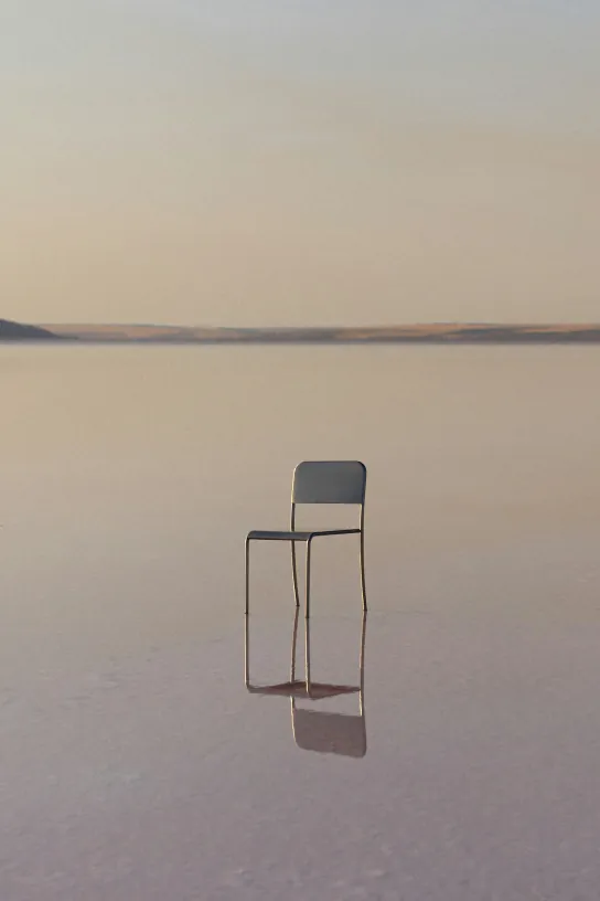 Single chair standing on a reflective salt flat under a hazy sky