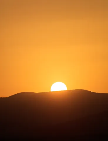 Sun setting behind a dark hill in an orange sky
