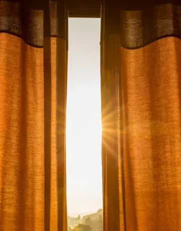 Sunlight streaming between orange linen curtains