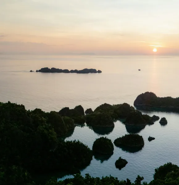 Sunset over a calm sea with small rocky islands and a wooded headland