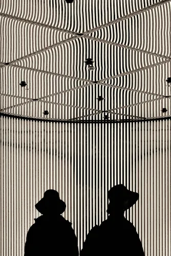 Silhouettes of two people in hats against a striped curved interior