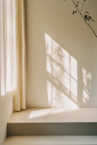 Sunlight from a window falling on a cream wall beside a sheer curtain