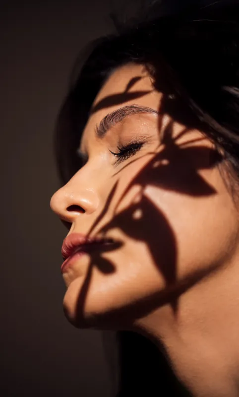 Profile of a woman with dark hair, leaf shadows across her face