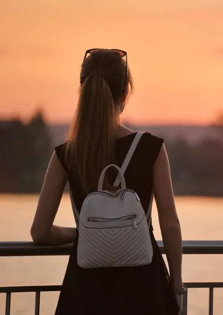 Woman with a ponytail and backpack at a railing watching the sunset over water