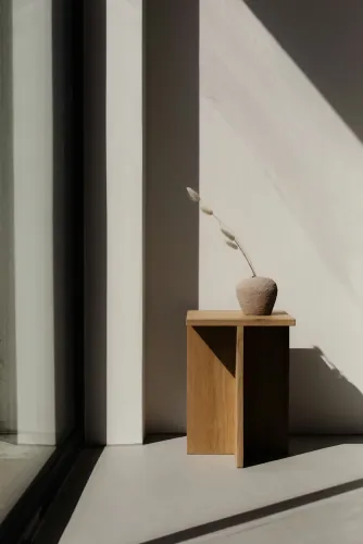Wooden stool with a small vase in sunlight beside a window